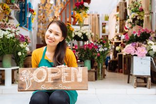 florista sonriendo y sosteniendo un letrero de abierto